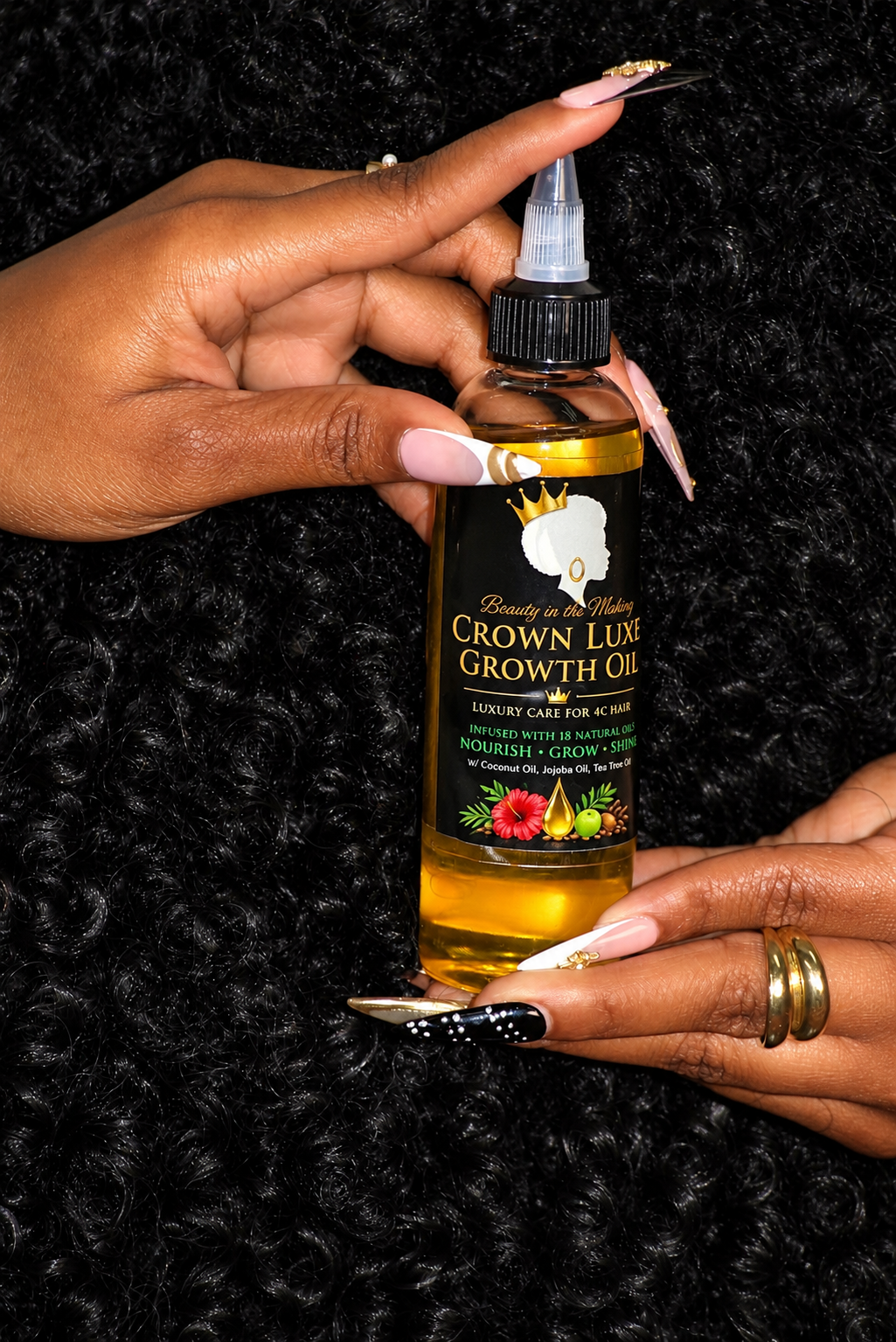 Close-up of Crown Luxe Growth Oil held in manicured hands against a black textured background